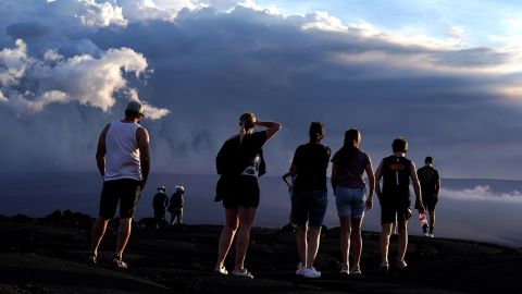 People stand on lava rock from a previous eruption near the Mauna Loa volcano as it erupts Wednesday near Hilo, Hawaii.