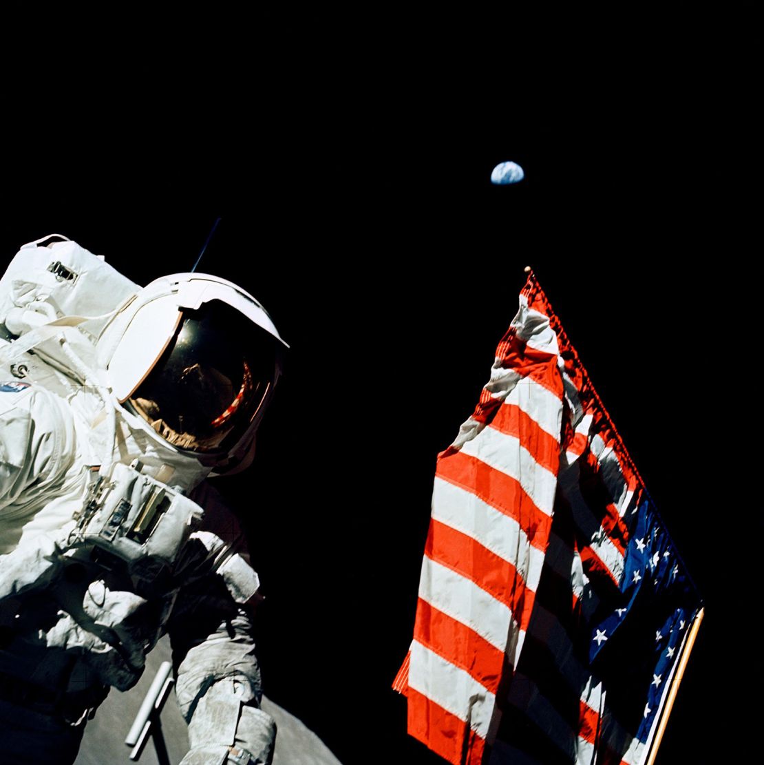 Astronaut Harrison Schmitt stands by the American flag during a moonwalk during Apollo 17, with Earth in the background.