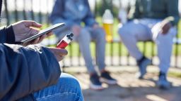Close Up Of Teenagers With Mobile Phone Vaping and Drinking Alcohol In Park