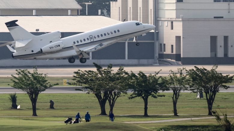 Golf players walk on a neighbouring golf course as a private jet, carrying the coffin of Australian cricket player Shane Warne, departs from Don Mueang Airport in Bangkok on March 10, 2022, on its way back to Australia after the cricketer died on the Thai holiday island of Koh Samui on March 4.