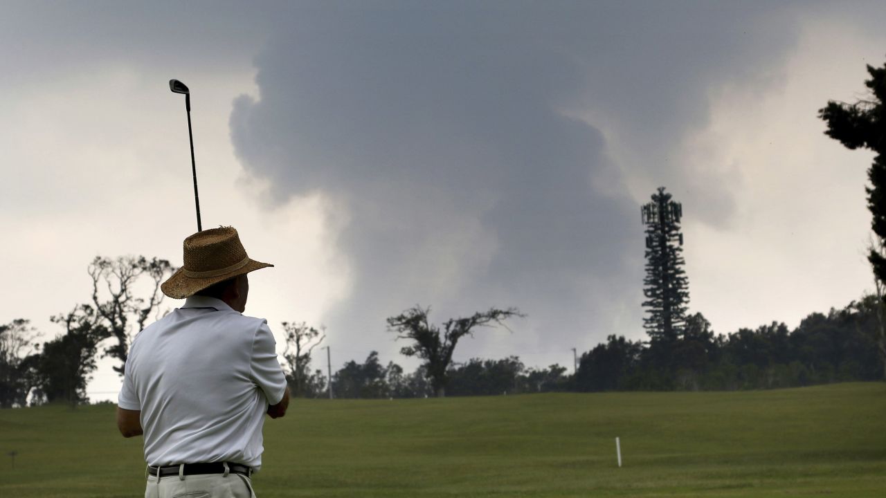 A golfer plays the Volcano Course as ash from the summit crater of Kilauea rises in the background, May 2018.