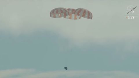 La capsula di Orione, con i suoi tre paracadute principali, si avvicina alla superficie dell'oceano.