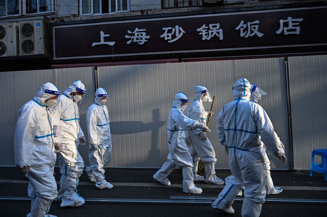 Workers in  protective clothes walk past barriers placed to close off streets in areas locked down after the detection of cases of Covid-19 in Shanghai on March 15, 2022.