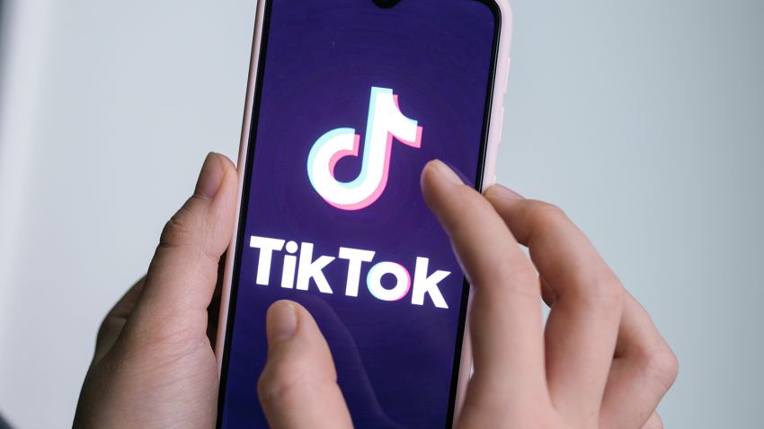 فتاة تمسك هاتفها الذكي مع شعار تطبيق الفيديو القصير TikTok في يديها.