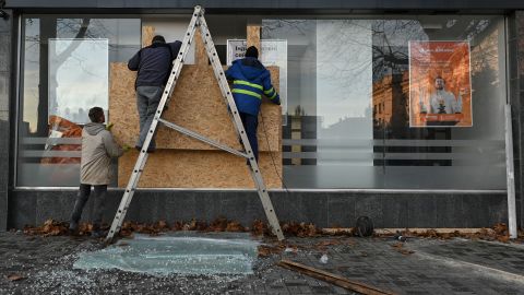 Мужчины вставляют деревянные доски в окно банка рядом со зданием Херсонской госадминистрации после ракетного обстрела города Херсона в среду.