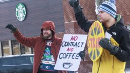 Anton Deborst, left, and Noah Zierhut, NBC members raise their fist and hold signs during the "Unfair Labor Practice Strike," on Friday, Dec. 16, 2022, in St. Anthony, Minn. Starbucks workers around the U.S. are planned a three-day strike starting Friday. The walkouts are part of their effort to unionize the coffee chain's stores. 