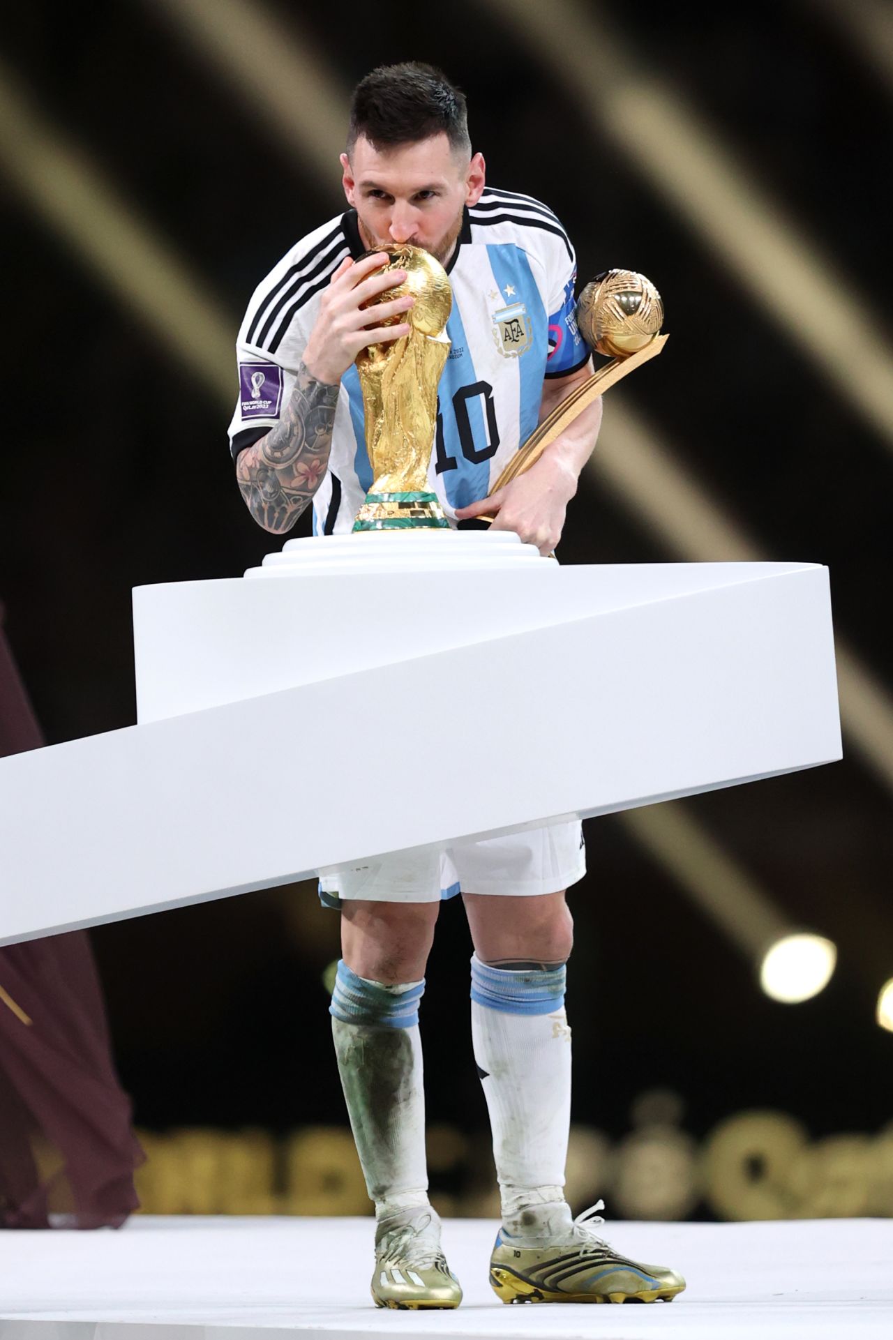 Messi holds the Golden Ball trophy, awarded to the tournament's top player, while kissing the World Cup trophy.
