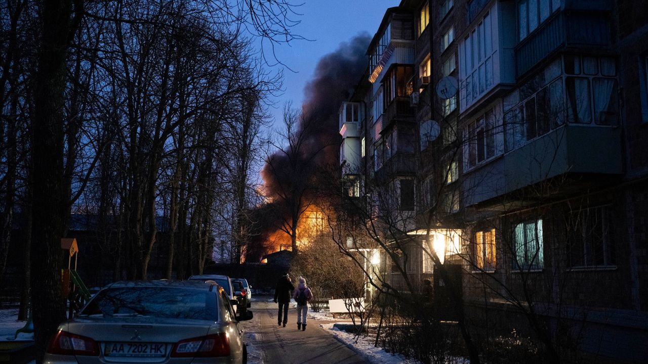 Residents watch a burning infrastructure project hit during a Russian drone strike in Kyiv on December 19, 2022. 