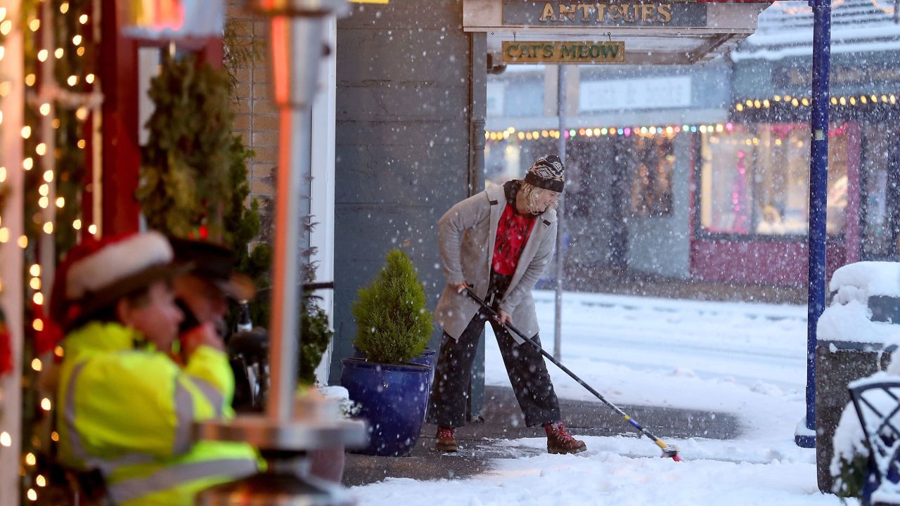 Kristin Jagodzinske sweeps the snow off the sidewalk in front of her shop in snowy downtown Poulsbo on Tuesday, Dec. 20, 2022.