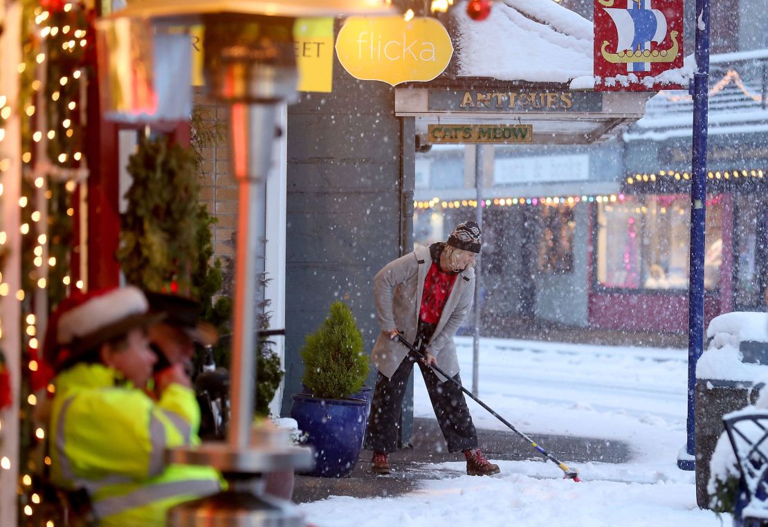 Kristin Jagodzinske sweeps the snow off the sidewalk in front of her shop in snowy downtown Poulsbo on Tuesday, Dec. 20, 2022.
