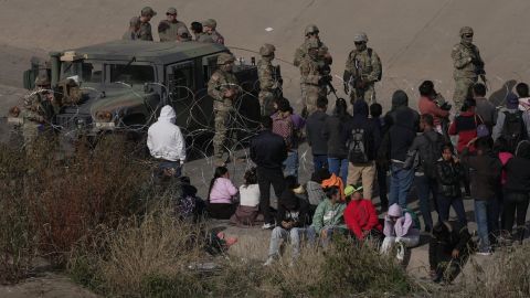 A group of migrants wait on the US side of the Rio Grande as the Texas National Guard blocked access to parts of the border with barbed wire and vehicles as seen from Ciudad Juarez, Mexico on December 20, 2022.