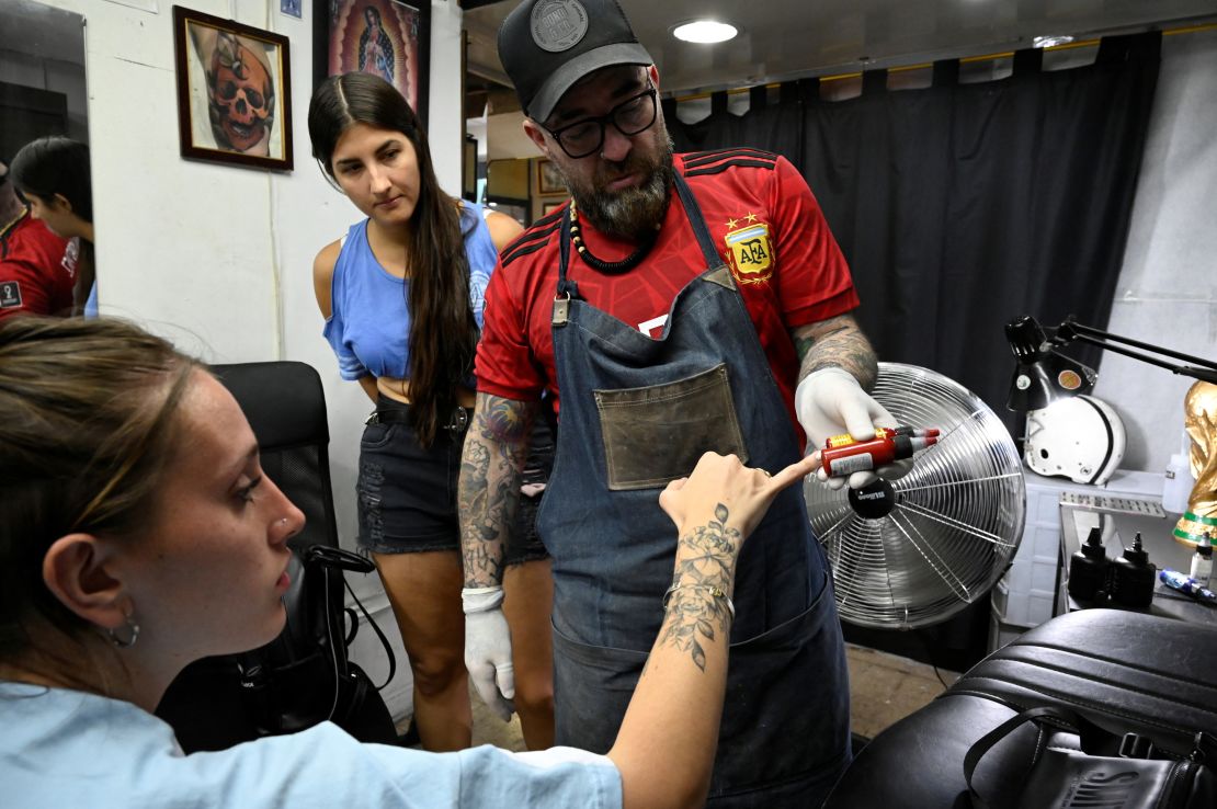 Sebastian Arguello Paz shows red ink to Florencia Sola, 26, before tattooing her with a number 10, honouring Messi.