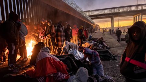 2022 年 12 月 22 日、テキサス州エルパソで、米国とメキシコの国境フェンスの隣で外で夜を過ごした後、明け方に火を温める移民たち。 