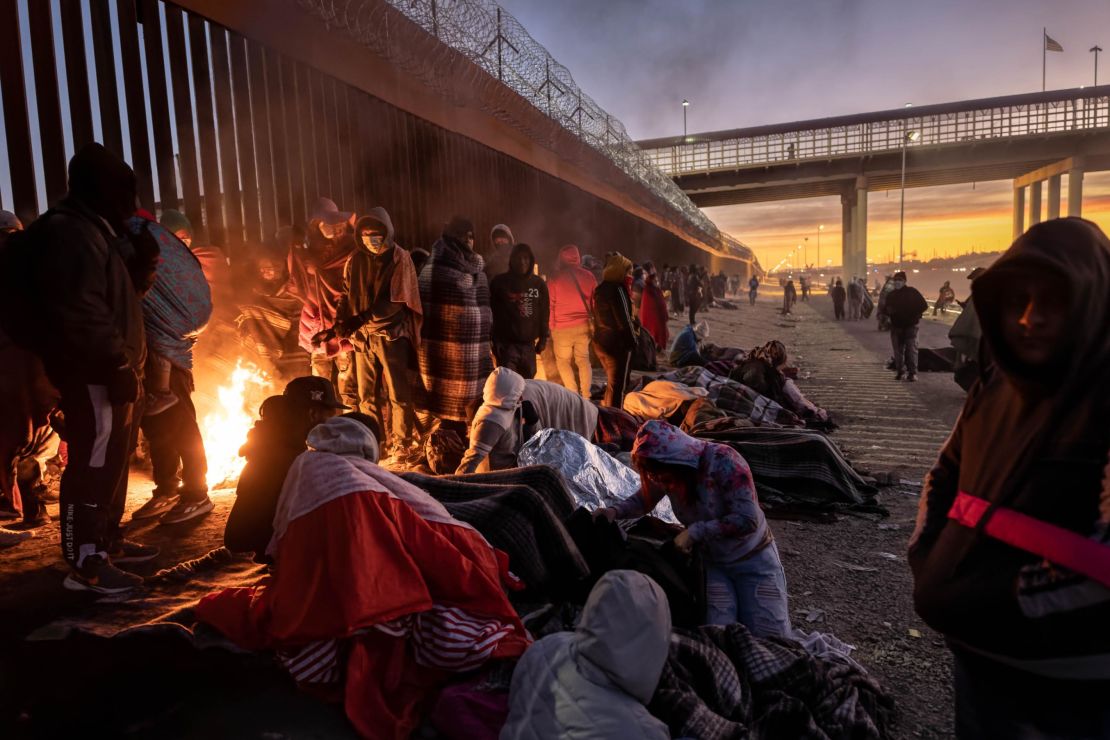 Migrants warm to a fire at dawn after spending the night outside next to the US-Mexico border fence on December 22, 2022, in El Paso, Texas. 