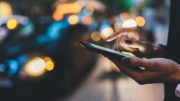 Businesswoman with smartphone using application for calling taxi online walking on city street night, female hands with internet connection texting friend via mobile phone on background bokeh color light