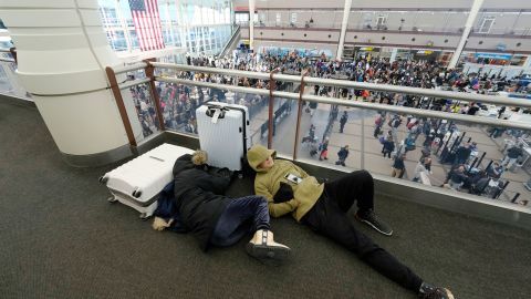 A pair of travelers sleep while others line up to pass through a security checkpoint in Denver International Airport on Friday. 