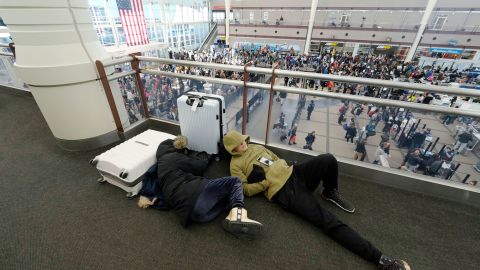 A pair of travelers sleep while others line up to pass through a security checkpoint in Denver International Airport on Friday.