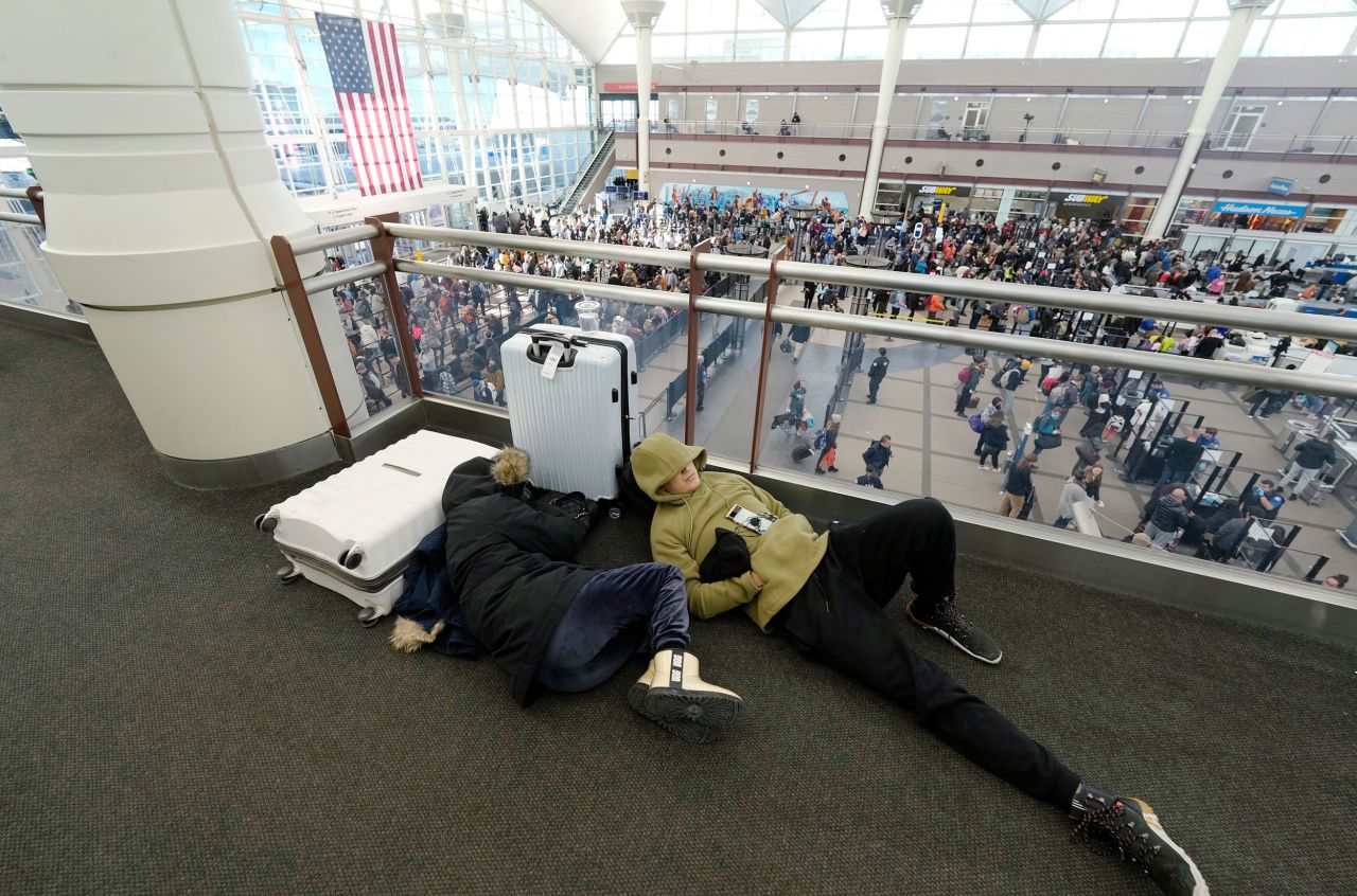 A pair of travelers sleep while lines of people pass through a security checkpoint at Denver International Airport.