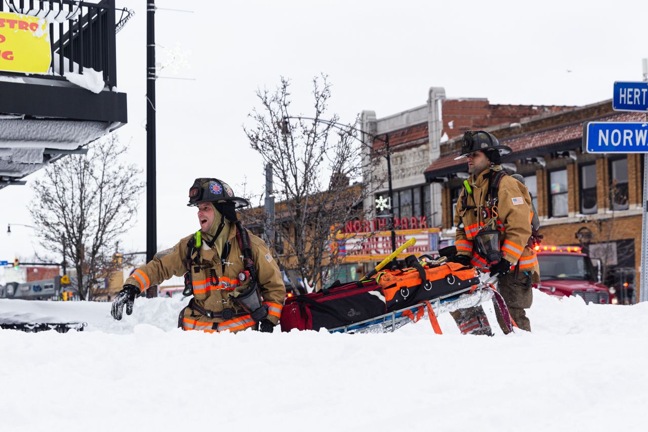 Firefighters carry rescue equipment as they respond to a fire on a snow-covered street in Buffalo on Sunday, December 25.