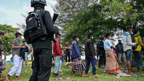 A policeman stands guard next to a group of Rohingya refugees waiting to be transferred to a temporary shelter following their arrival by boat in Krueng Raya, Indonesia's Aceh province on December 25, 2022.
