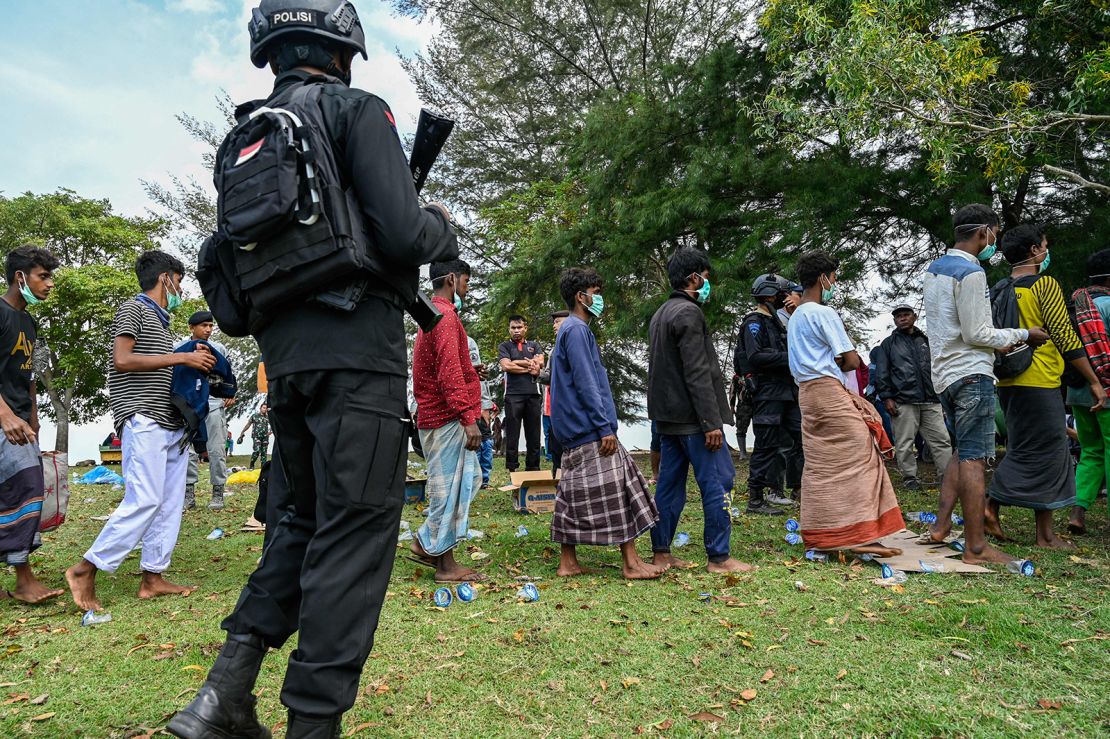 A policeman stands guard next to a group of Rohingya refugees waiting to be transferred to a temporary shelter following their arrival by boat in Krueng Raya, Indonesia's Aceh province on December 25, 2022. 