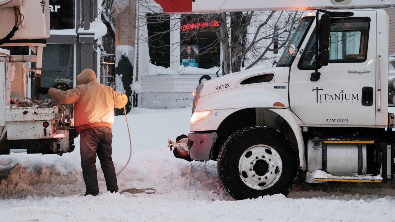 A utility worker straps a rope to a truck in an attempt to tow another in Buffalo, New York, on Monday. 