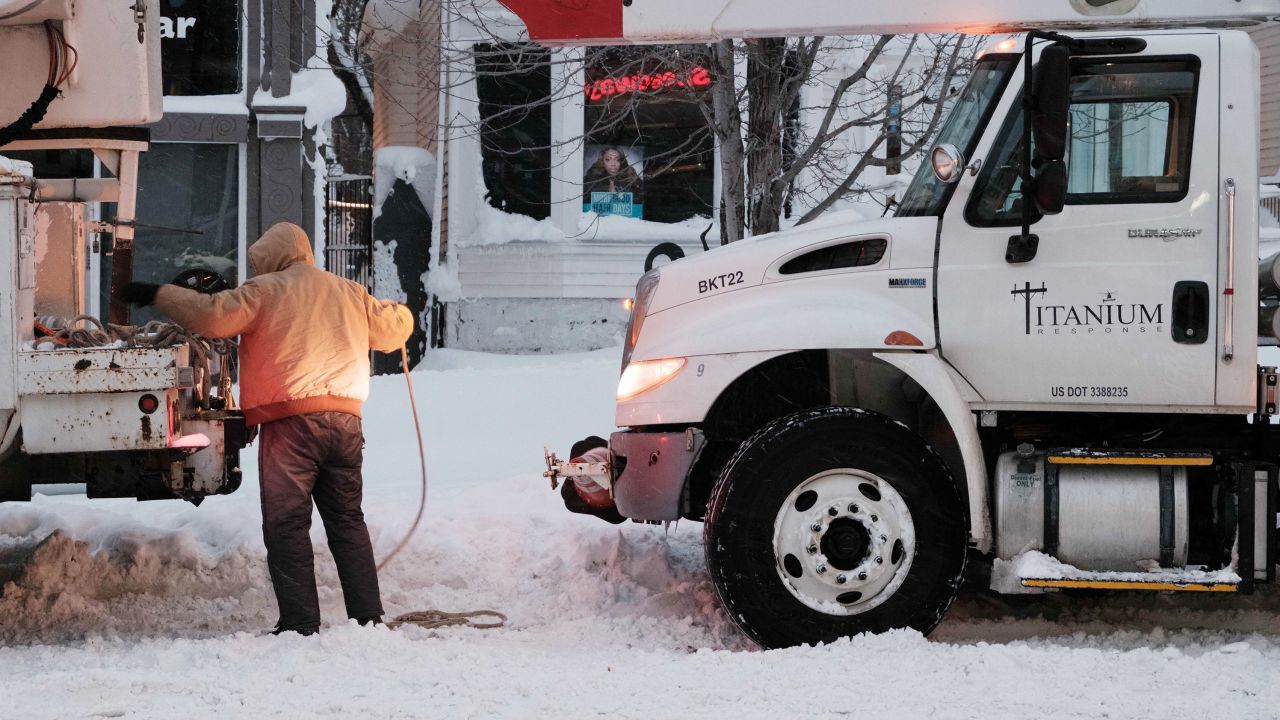 A utility worker straps a rope to a truck in an attempt to tow another in Buffalo, New York, on Monday.