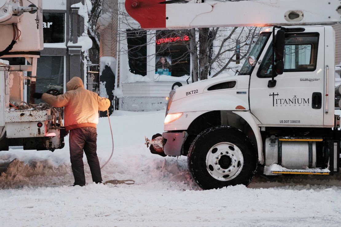 A utility worker straps a rope to a truck in an attempt to tow another in Buffalo, New York, on Monday. 