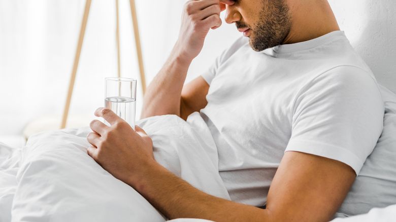 cropped view of man with headache holding glass of water in bed 