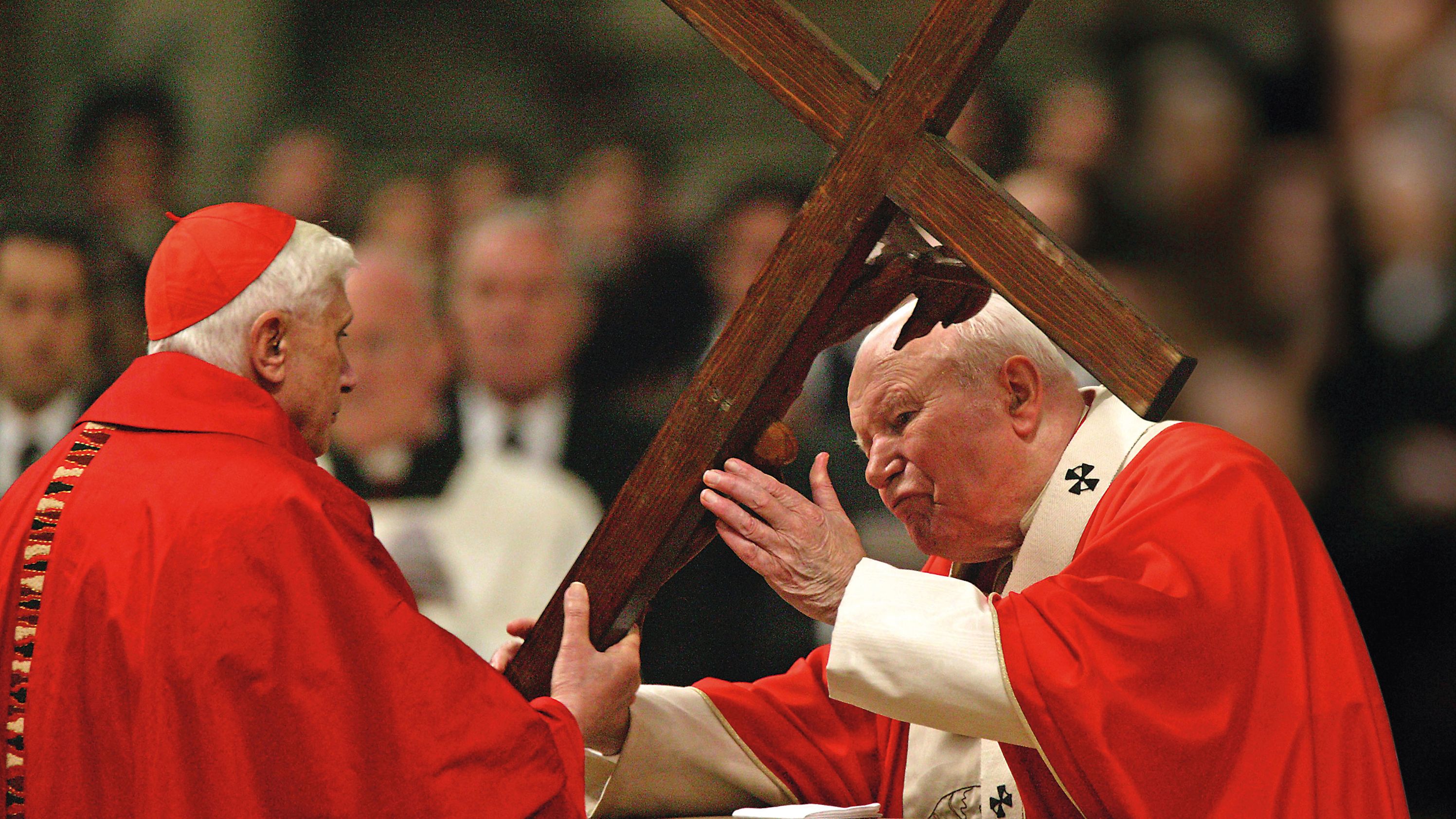 Benedict passes a cross to Pope John Paul II during a Passion of Christ celebration at the Vatican in the 2000s.
