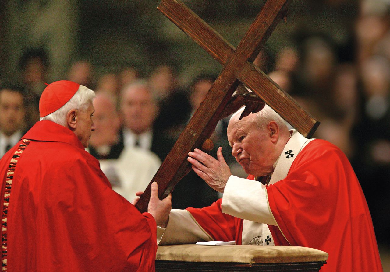 Benedict passes a cross to Pope John Paul II during a Passion of Christ celebration at the Vatican in the 2000s.
