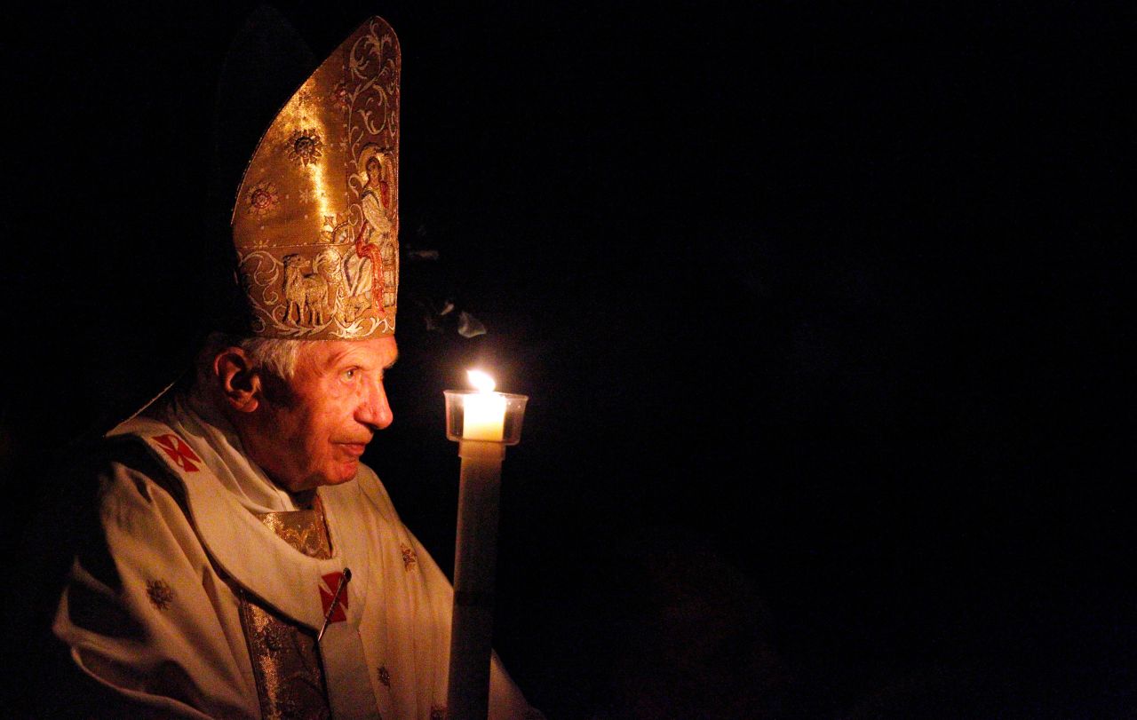 Benedict, holding a candle, enters a hushed and darkened St. Peter's Basilica to begin the Vatican's Easter vigil service in April 2012.