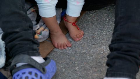 Brenda's tiny feet wear a rosary as she stands on the asphalt of an El Paso parking lot.
