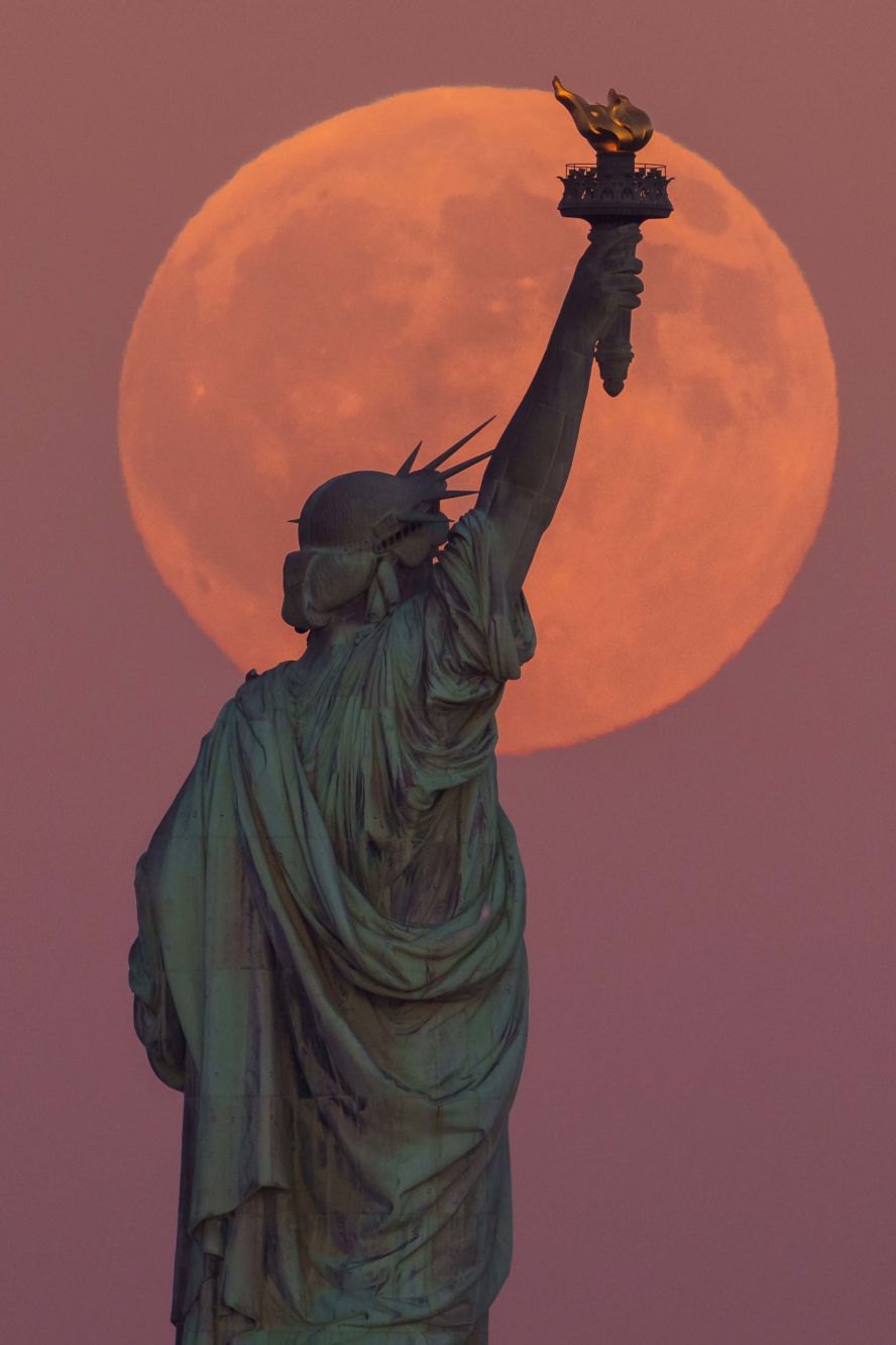 The full moon is seen behind the Statue of Liberty in New York on Monday, October 6.