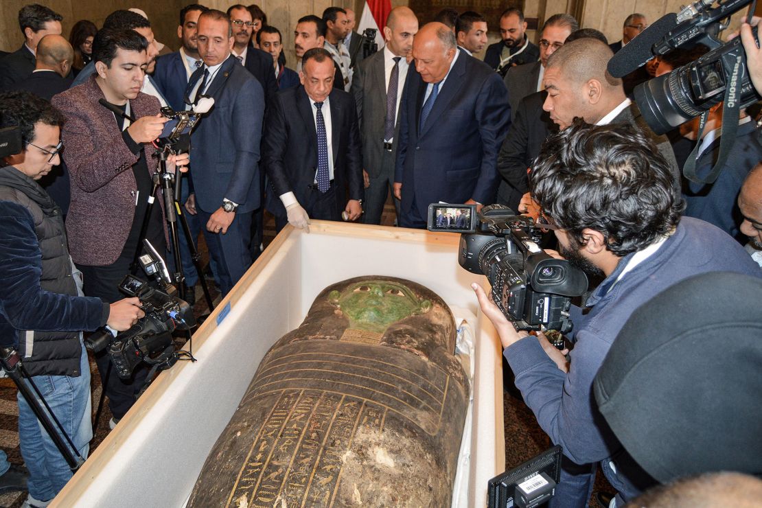 Egyptian Foreign Minister Sameh Shoukry and head of Egypt's Supreme Council of Antiquities Mostafa Waziri are surrounded by journalists as they inspect a wooden sarcophagus, which was handed over by the US in a ceremony on Monday in Cairo, Egypt.  