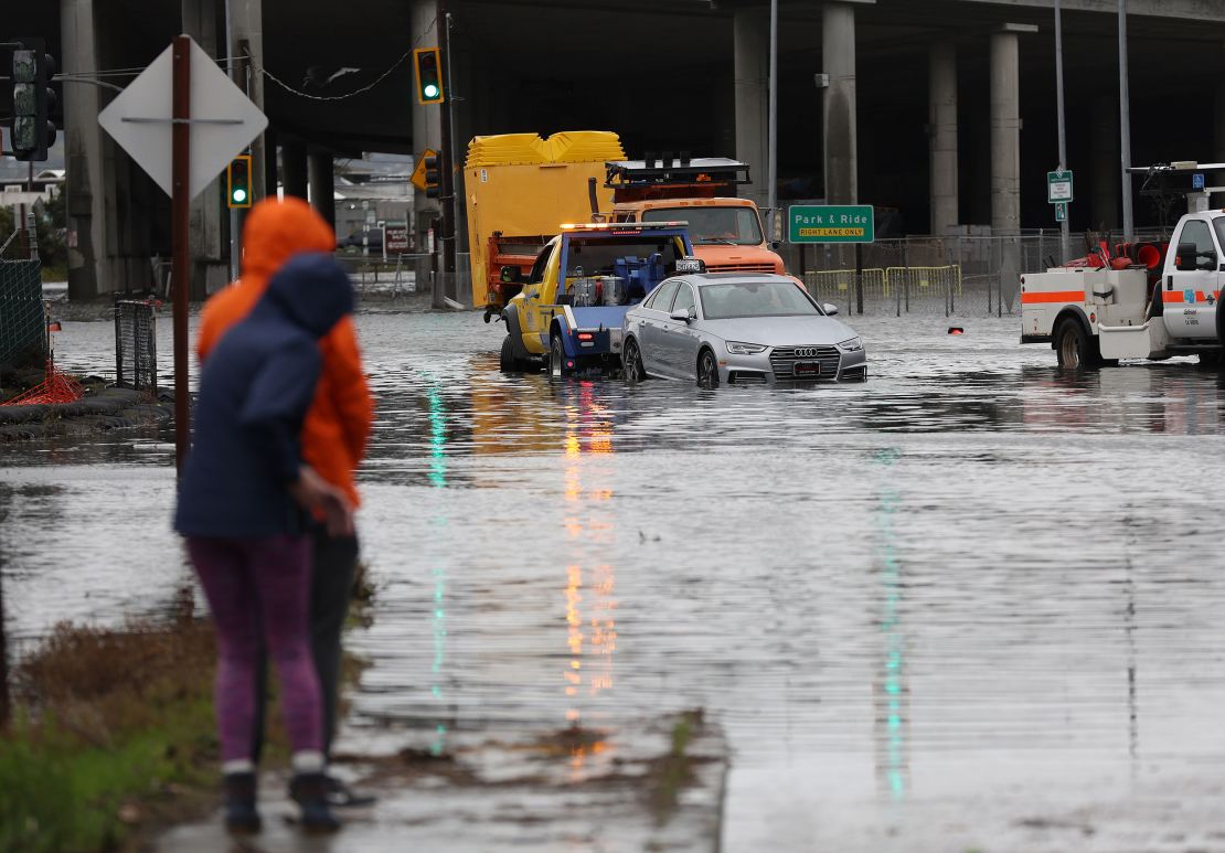 People look on as a tow truck pulls a car out of a flooded intersection on January 4, 2023, in Mill Valley, California. 