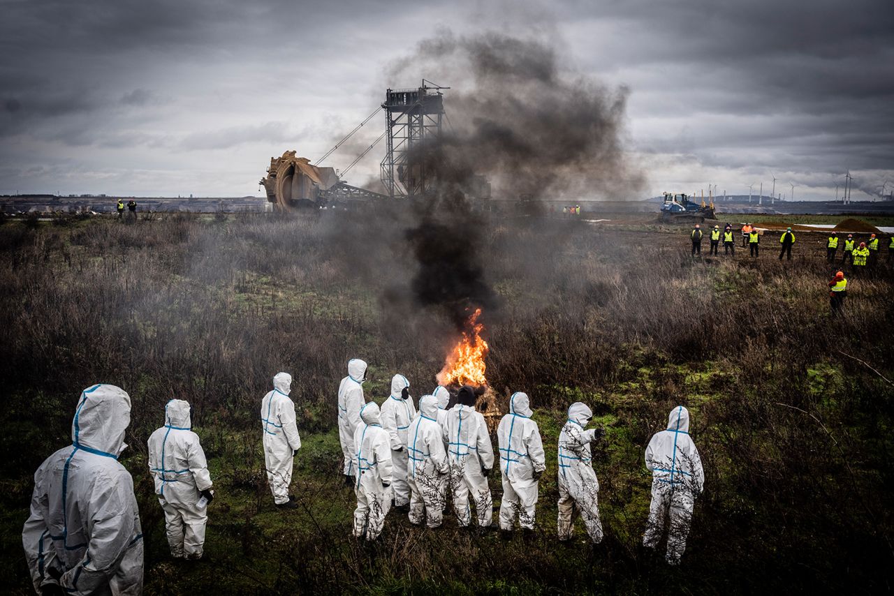 Activists clad in white overalls watch a fire burn in front of a bucket-wheel excavator in Lützerath, Germany, on Monday, January 2. The village is located on the edge of the still expanding Garzweiler II lignite surface. Despite heavy protests, it will soon be demolished to extract the underlying coal.