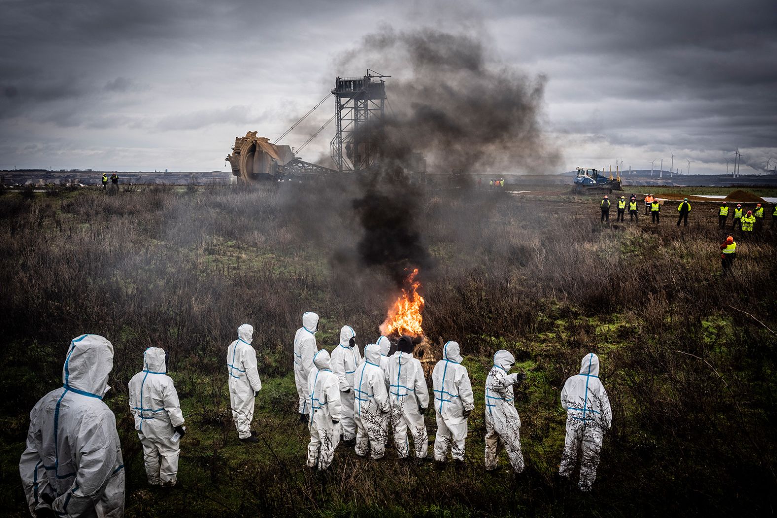 Activists clad in white overalls watch a fire burn in front of a bucket-wheel excavator in Lützerath, Germany, on Monday, January 2. The village is located on the edge of the still expanding Garzweiler II lignite surface. Despite heavy protests, it will soon be demolished to extract the underlying coal.