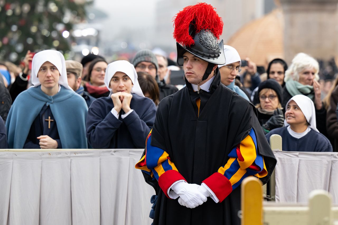 Mourners attend the public funeral mass for Pope Emeritus Benedict XVI in St. Peter's Square, preceded by a member of the Pontifical Swiss Guard.