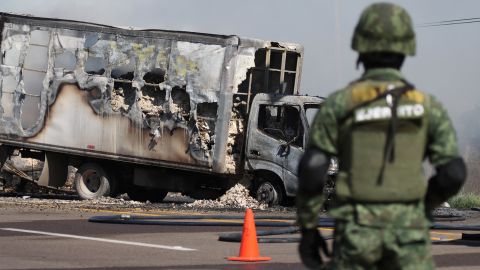 A soldier keeps watch near the wreckage of a truck set on fire by drug gang members in Sinaloa, following Guzmán's detention by Mexican authorities.