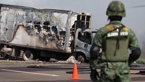 A soldier stands guard near the wreckage of a truck burned by drug cartel members in Sinaloa, after Guzmán was detained by Mexican authorities.