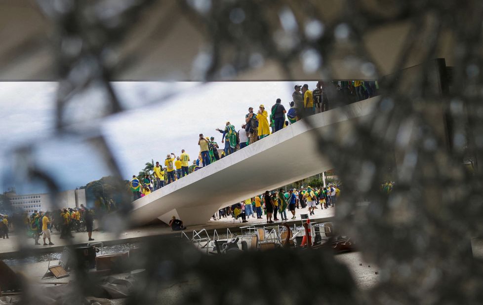 Supporters of former President Jair Bolsonaro are pictured through broken glass as they hold a demonstration.