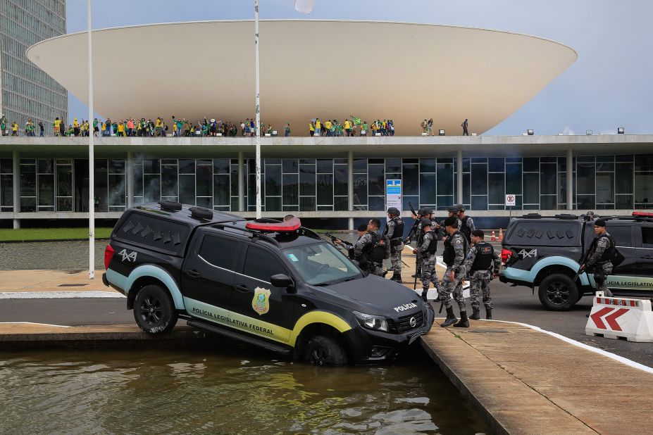 Members of the Federal Legislative Police stand next to a vehicle that crashed into a fountain outside the National Congress in Brasilia.