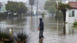 A man wades through a flooded street in the Rio Del Mar neighborhood of Aptos, California, January 9, 2023. 