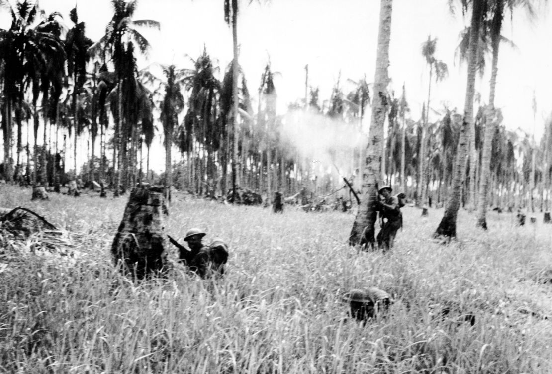 Australian forces advance through a coconut grove and kunai grass in Japanese-occupied New Guinea in February 1943 during World War II.