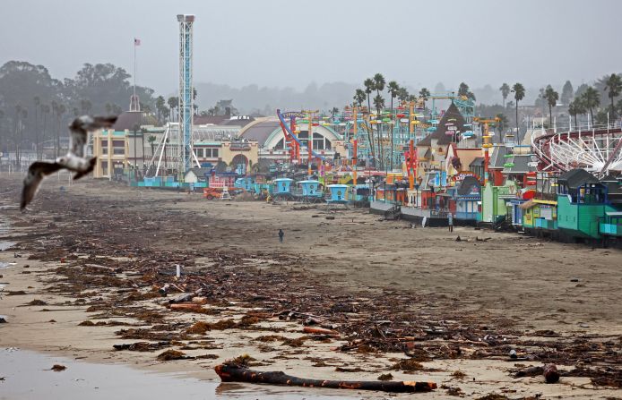 A person walks near driftwood and storm debris that washed up in front of the Santa Cruz Beach Boardwalk amusement park.