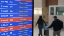 Travelers walk as a video board shows flight delays and cancellations at Ronald Reagan Washington National Airport in Arlington, Va., Wednesday, Jan. 11, 2023. 