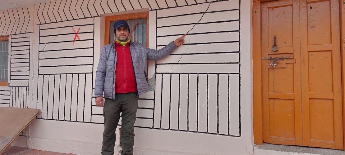 Suraj Kaparuwan points to a crack in his house, which is marked X because it's considered too dangerous to occupy.