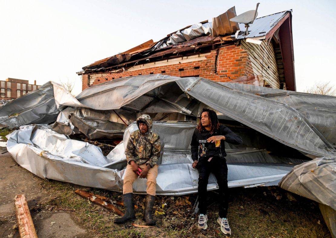 Cordel Tyus and Devo McGraw sit on roofing that blew off of an industrial building and wrapped around their house Thursday after a tornado ripped through Selma, Alabama. 