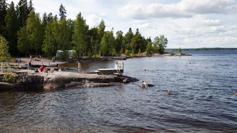 फिनलैंड की एक झील के किनारे प्रकृति का लुत्फ उठाते लोग।   